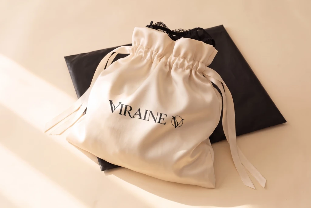 VIRAINE satin pouch in cream with black logo, on a plain black outer bag